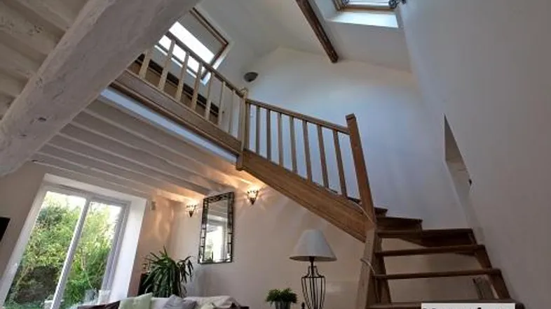 Helles Wohnzimmer mit offener Holztreppe, hohen Decken, Dachfenstern und Blick in den Garten.