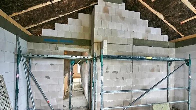 Innenansicht eines Rohbaus mit unverputzten Wänden, Dachisolierung und Gerüst im Bau.