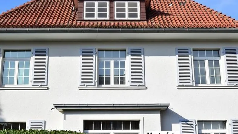 Klassische Hausfassade mit roten Dachziegeln, weißen Fensterläden und Gaubenfenstern unter blauem Himmel.