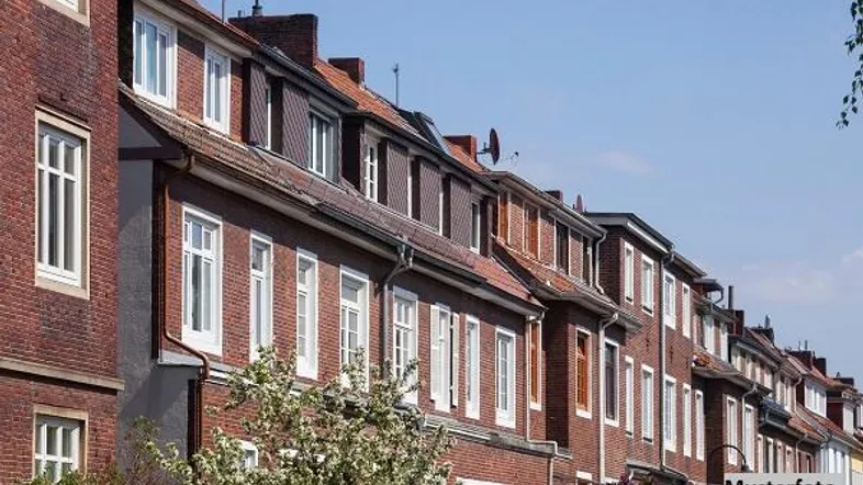 Reihenhäuser mit roten Backsteinfassaden und weißen Fenstern unter blauem Himmel, gut gepflegt.