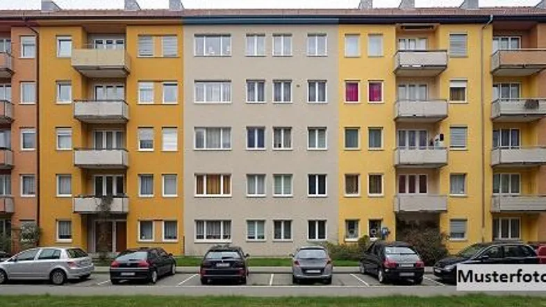 Mehrfamilienhaus mit gelber und beiger Fassade, mehreren Balkonen und parkenden Autos davor.