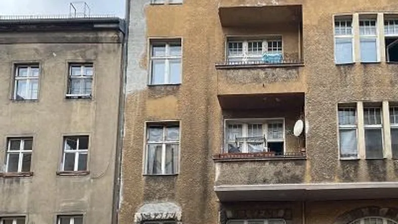 Fassade eines älteren Mehrfamilienhauses mit Balkonen und sichtbaren Gebrauchsspuren.