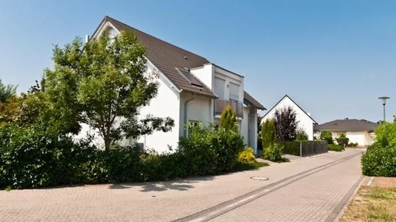 Weißes Einfamilienhaus mit Satteldach, gepflegter Außenanlage und blauer Himmelkulisse.