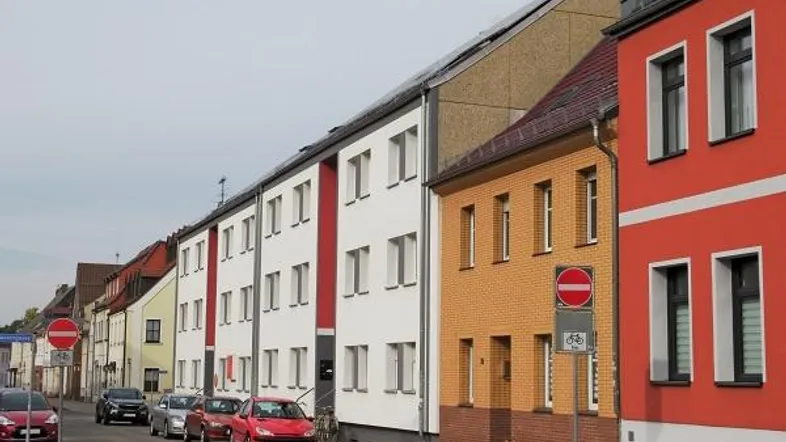 Reihenhäuser in einer städtischen Umgebung mit verschiedenen Fassadenfarben und parkenden Autos auf der Straße.