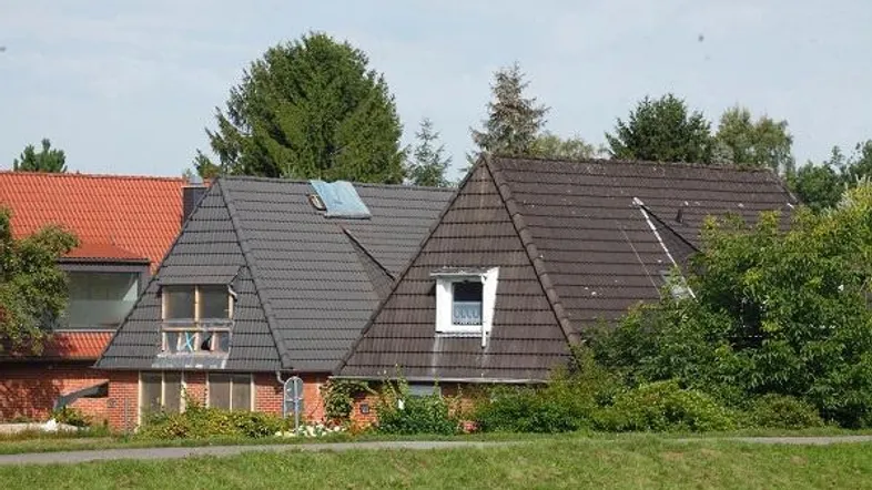 Außenansicht von zwei Häusern mit Satteldächern und Gaubenfenstern, umgeben von Grünflächen.