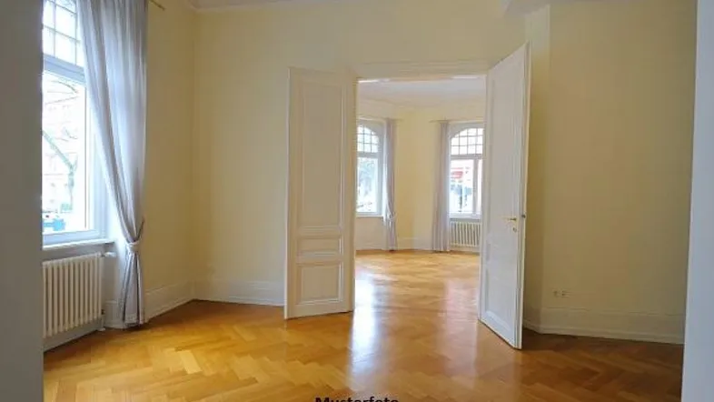 Helles Zimmer mit Fischgrätparkett, hohen Decken und großen Fenstern, typisch für einen Altbau.