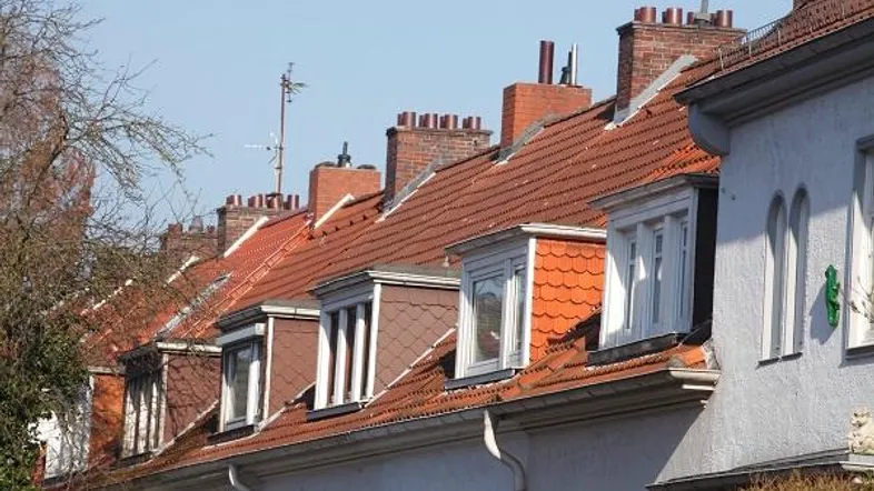 Reihe von Wohnhäusern mit roten Ziegeldächern, Gaubenfenstern und Schornsteinen unter blauem Himmel.