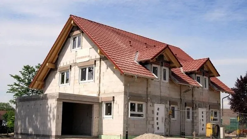 Neubau eines Doppelhauses im Rohbau mit rotem Satteldach und integrierter Garage.