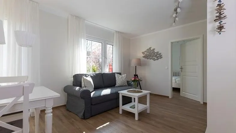 Helles Wohnzimmer mit einem bequemen Sofa, Couchtisch und Laminatboden, mit Zugang zu einem weiteren Raum.