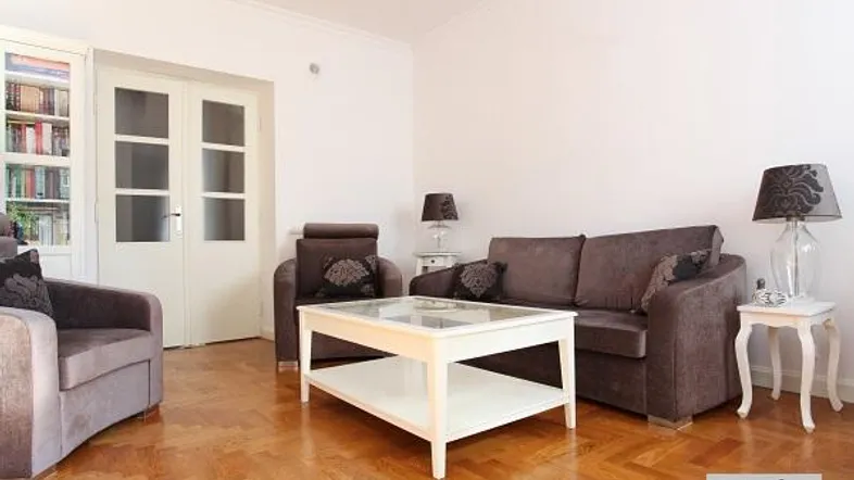 Helles Wohnzimmer mit elegantem Parkettboden, bequemen Sofas und einem Bücherregal.