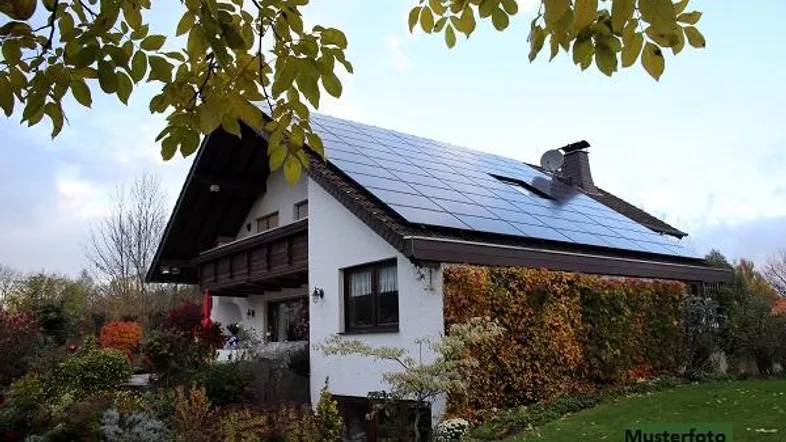 Haus mit Solaranlage auf dem Dach, umgeben von einem herbstlichen Garten mit Bäumen.