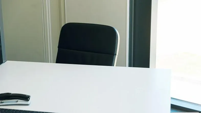 Modernes Büro mit weißem Schreibtisch, schwarzem Bürostuhl und viel Tageslicht durch das Fenster.