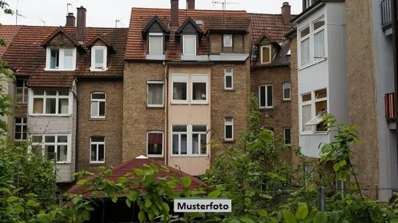 Historisches Mehrfamilienhaus mit Ziegelfassade, Gaubenfenstern und rotem Ziegeldach, umgeben von üppigem Grün.