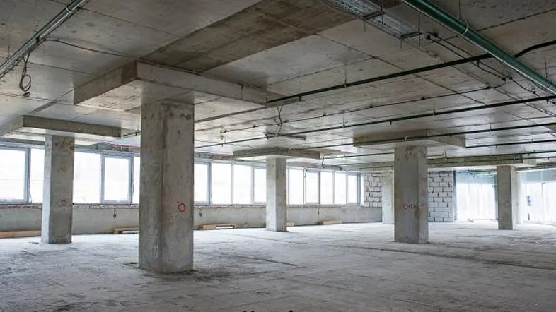 Großer, unfertiger Innenraum mit Betonstützen, hohen Decken und vielen Fenstern für natürliches Licht.