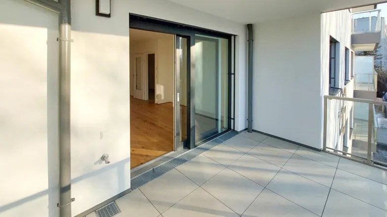 Heller Balkon mit Fliesenboden und Zugang zu einem Innenraum mit Holzparkett.