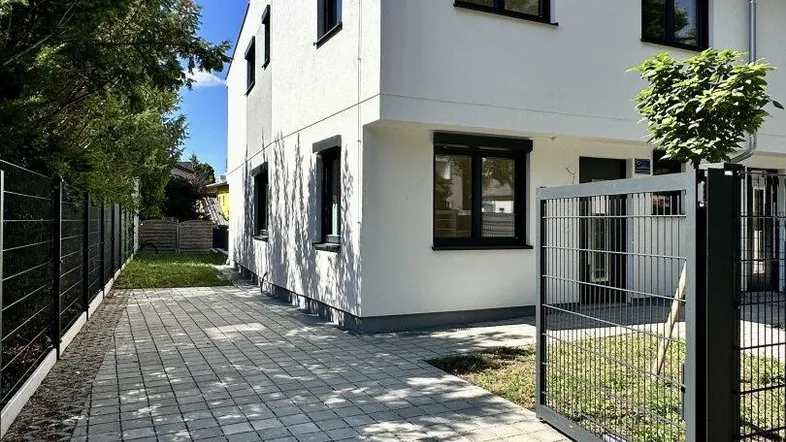 Moderne weiße Doppelhaushälfte mit gepflasterter Einfahrt und schwarzem Zaun unter blauem Himmel.