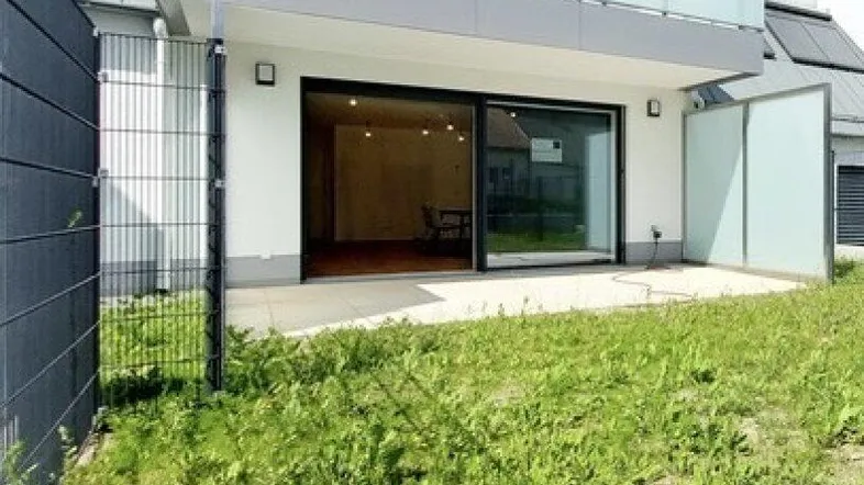 Moderne Wohnanlage mit Erdgeschoss-Terrasse und angrenzender Grünfläche unter einem Balkon.