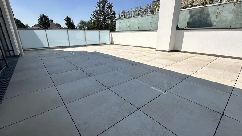 Geräumige, sonnige Dachterrasse mit modernen Fliesen und Glasgeländer, ideal zum Entspannen.