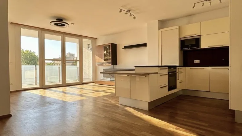 Helles, offenes Wohnzimmer mit integrierter Küche, Parkettboden und Zugang zum Balkon.