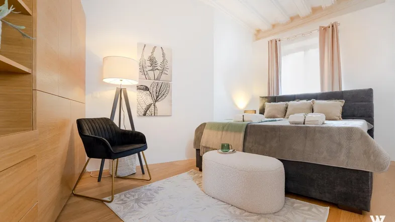 Helles Schlafzimmer mit Doppelbett, Holzfußboden und moderner Einrichtung unter hohen Decken.