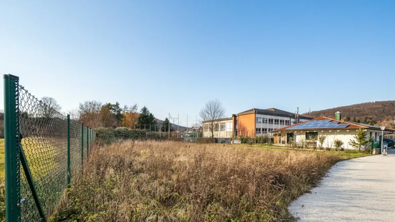 Weitläufiges Grundstück mit Blick auf umliegende Gebäude, Sportanlagen und grüne Hügel unter klarem Himmel.