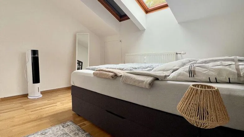 Helles Schlafzimmer im Dachgeschoss mit Holzboden, gemütlichem Bett und großen Dachfenstern.