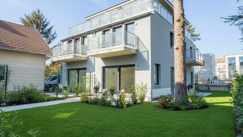 Modernes Mehrfamilienhaus mit gepflegtem Vorgarten, Balkonen und Dachterrasse unter blauem Himmel.