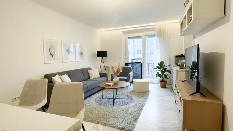 Helles Wohn- und Esszimmer mit modernem Sofa, Esstisch und Zugang zum Balkon.
