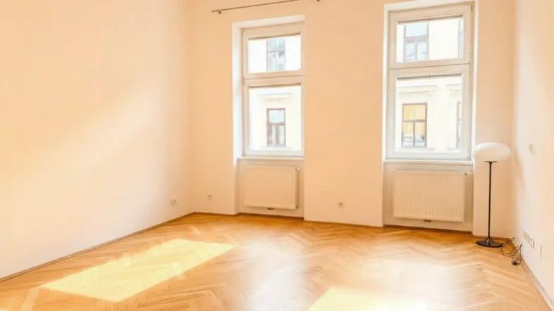 Heller Wohnraum mit Fischgrätparkettboden und großen Fenstern, die viel Tageslicht hereinlassen.