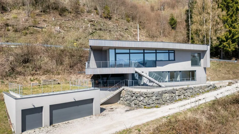 Modernes Haus mit Flachdach und Doppelgarage in Hanglage mit Bergblick.