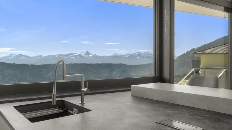 Moderne Küche mit dunkler Arbeitsplatte und Spüle, die einen weiten Blick auf die Berglandschaft bietet.