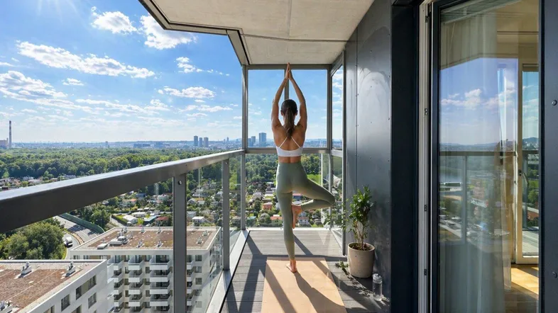 Sonniger Balkon mit weitem Stadtblick, Glasbrüstung und modernem Holzboden, ideal für Entspannung.