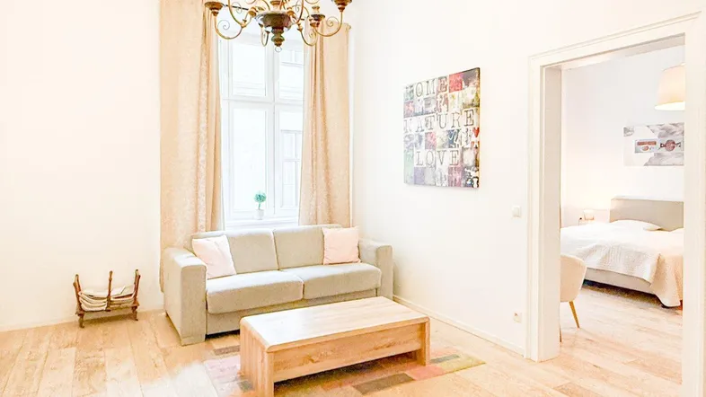 Helles Wohnzimmer mit Parkettboden, Kronleuchter und Zugang zu einem Schlafzimmer.