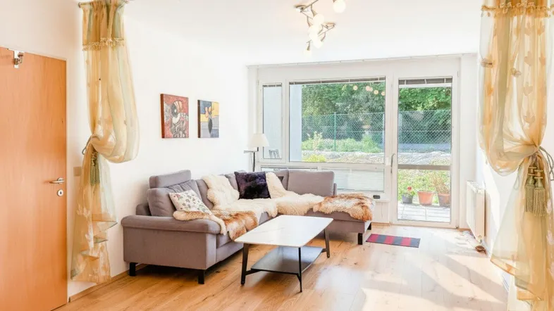Helles Wohnzimmer mit Holzboden, bequemer Couch und Zugang zum Gartenbereich.