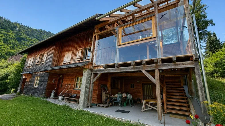 Holzhaus mit moderner Glaserweiterung und Bergblick in ländlicher Umgebung.