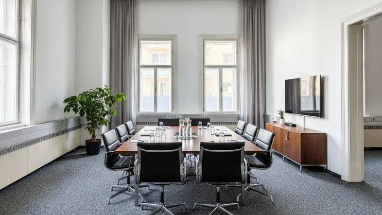 Geräumiger Konferenzraum mit großem Holztisch, modernen Stühlen und viel Tageslicht durch hohe Fenster.