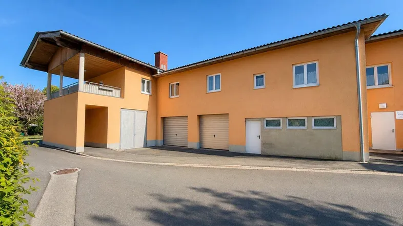 Seitenansicht des Gebäudes mit mehreren Garagentoren und einem überdachten Balkonbereich im Obergeschoss.