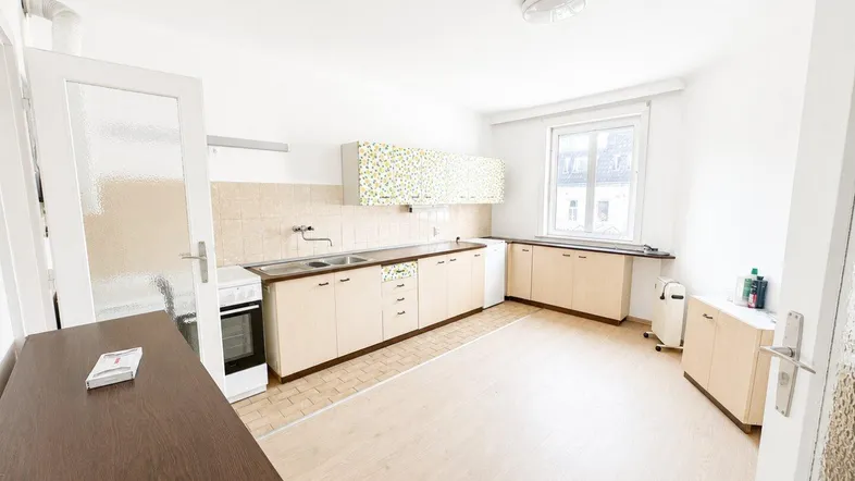 Helle Küche mit älteren Einbaumöbeln, Fliesenboden im Kochbereich und Fenster.