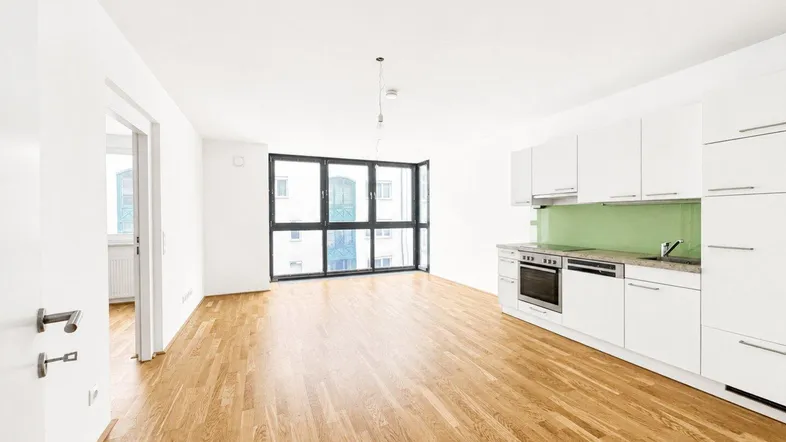 Helles, offenes Wohnzimmer mit integrierter Küche, Parkettboden und großen Fenstern.