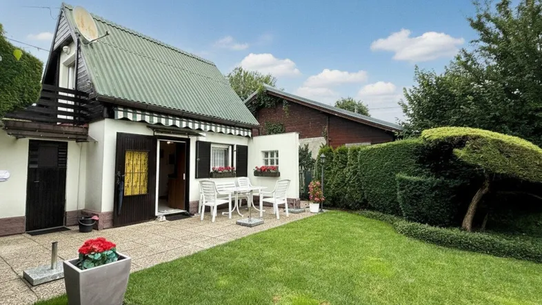 Kleines Haus mit grüner Dachfläche, einer möblierten Terrasse und gepflegtem Rasenbereich.
