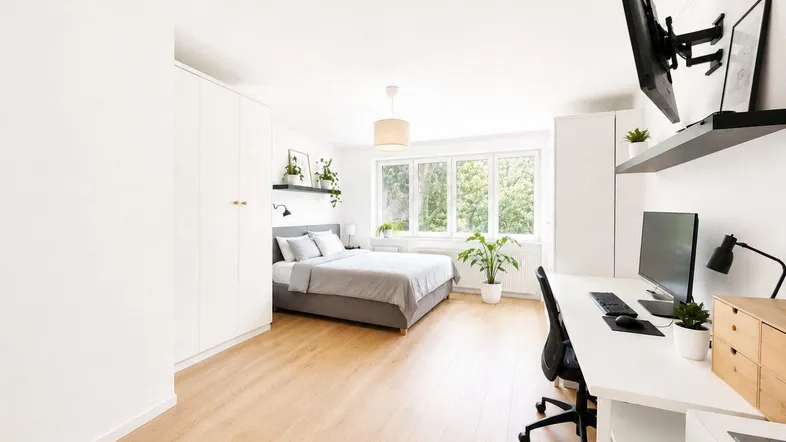 Helles Schlafzimmer mit Holzboden, großem Fenster und integriertem Arbeitsbereich.