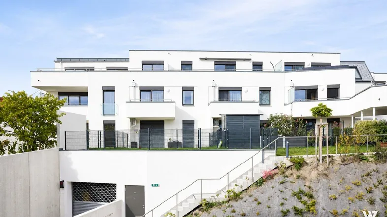 Moderne Wohnanlage mit weißer Fassade, Terrassen und Zugang zur Tiefgarage.