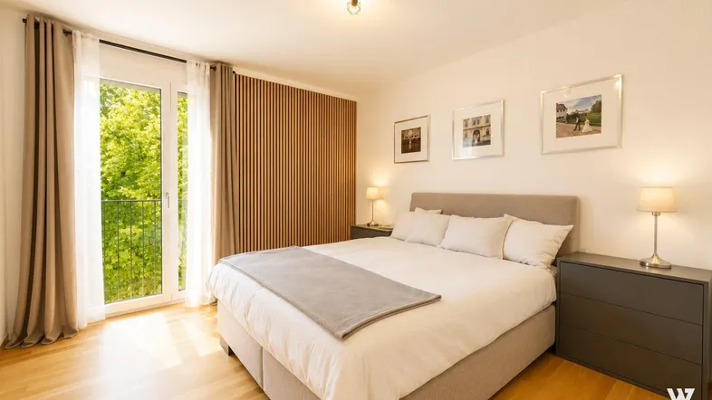 Gemütliches Schlafzimmer mit Doppelbett, Holzboden und Zugang zu einem französischen Balkon mit Grünblick.