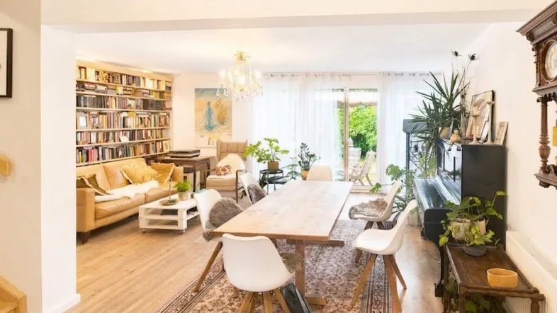 Helles und offenes Wohn-Esszimmer mit großem Esstisch, Bücherregal und Zugang zum Garten.