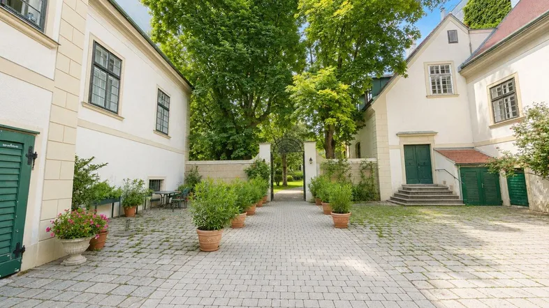 Historischer Innenhof mit gepflastertem Weg, umgeben von eleganten Gebäuden und altem Baumbestand.
