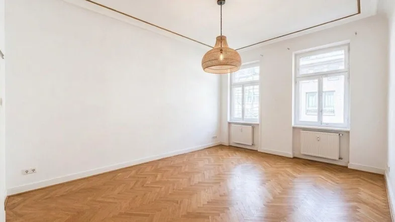 Helles Zimmer mit Fischgrätparkett, hohen Decken und dekorativer Deckenleiste, ideal als Wohn- oder Schlafzimmer.