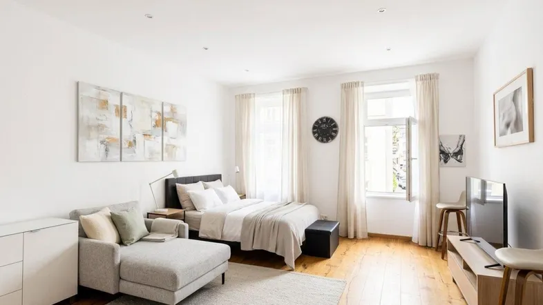 Helles Schlafzimmer mit Holzboden, großem Fenster und moderner Einrichtung, ideal für ein Studio-Apartment.