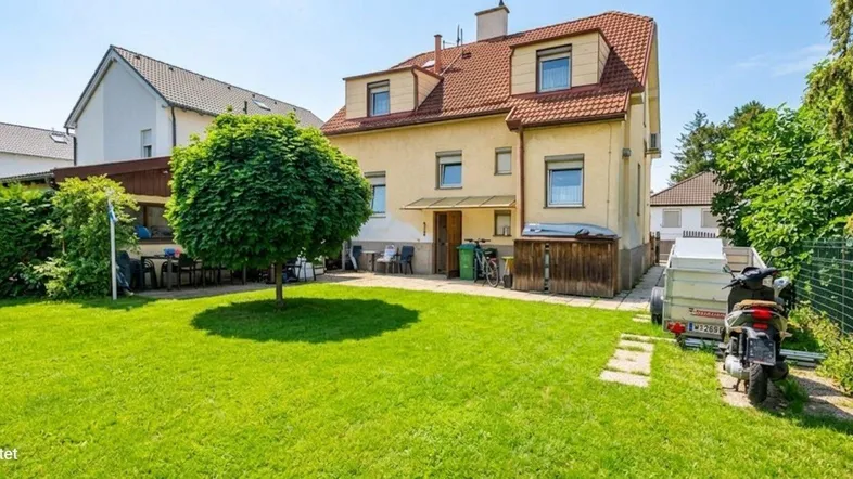 Großer, gepflegter Garten mit Rasenfläche, Baum und Sitzbereich hinter dem Haus.
