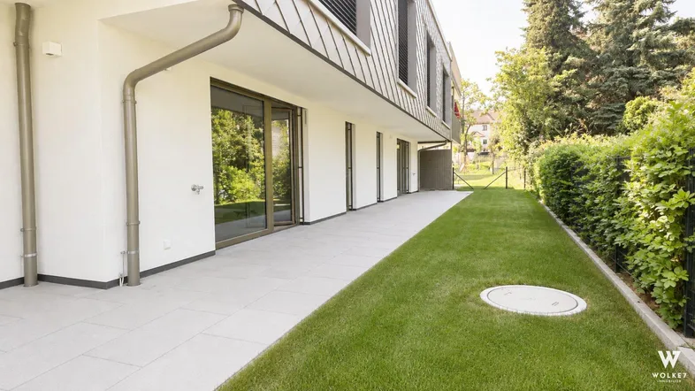 Moderne Gebäudefassade mit großer gepflasterter Terrasse und angrenzendem grünen Rasenbereich.