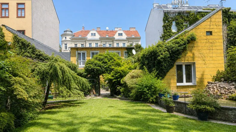 Großer, gepflegter Garten mit Rasenfläche und üppiger Bepflanzung, umgeben von charmanten Gebäuden.